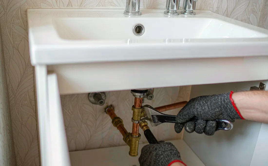 Gloved hands repairing pipework under a basin in a Tianhe apartment